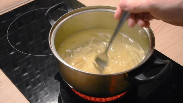 Boiling water in a metal saucepan and cooking long pasta macaroni spaghetti in water, stirring with a fork