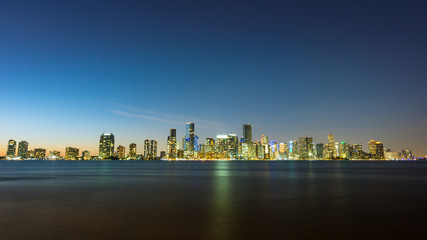 USA, Florida, Bright shining night skyline of miami with reflections on water and starry sky