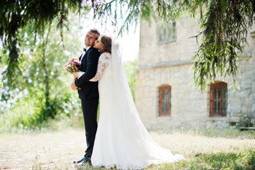 Romantic lovely newly married couple posing in the park by the medieval castle on their wedding day.