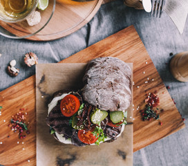 beautiful serving of rye ciabatta with beef, lettuce and sun-dried tomatoes on a wooden board with...