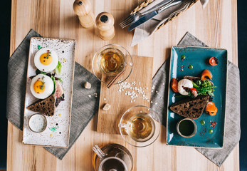 a beautifully layout breakfast arrangement with two plates: with egg poached, rye bread and salmon and tea and an English breakfast with fried eggs and bacon on a wooden table - 186574679