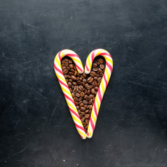 cane candies in heart shape with coffee beans flat view on black background