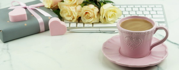 Valentine's day concept. Pink cup with cocoa, a bouquet of beautiful roses, a keyboard and a gift with pink hearts. Copy space. banner