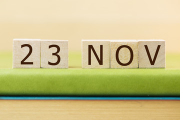 Wooden cube shape calendar for NOV 23 on green book, table.