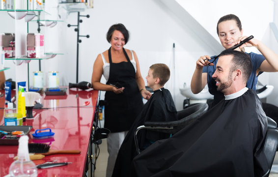 Glad female hairdresser cutting male client