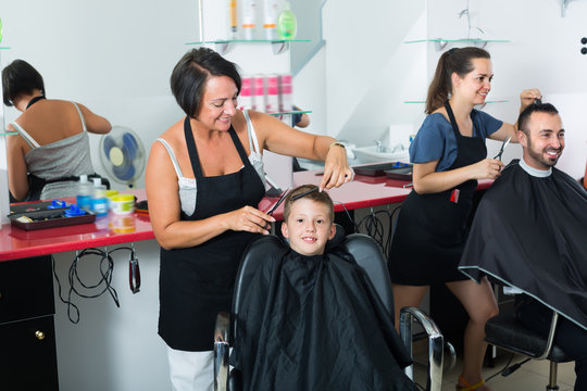 Little boy sitting in chair and getting hair cut