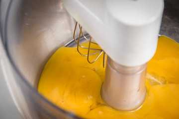 A kitchen mixer beating yellow egg yolks for fresh cake dough in a modern kitchen. - 186578080