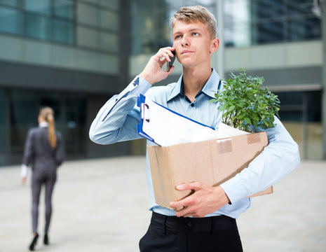 Young businessman with box is talking phone and searching new job