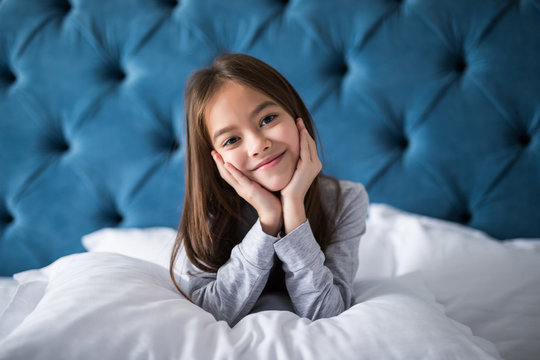 cute smiling little girl woke up in white bed holding pillow