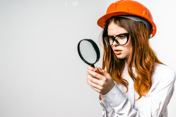 A woman builder in a hard hat looks into a magnifier