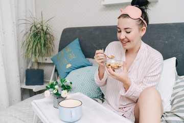 Young beautiful woman has breakfast in bed and eating cereals or muesli in the morning