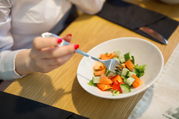 girl eating fork with fresh salad of cucumbers and tomatoes in a restaurant