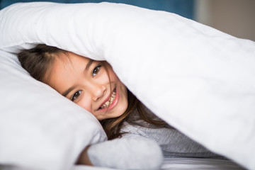 Fototapeta premium girl lying under a blanket in the bed and smiling at home
