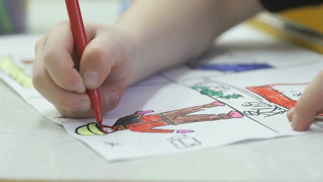 Close-up of unknown little child draws and paints pictures with felt-tip sitting at desk in the kindergarten