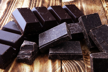 Dark brown chocolate pieces, stacks culinary wooden background.