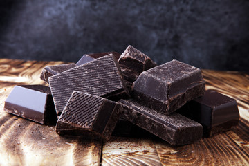 Dark brown chocolate pieces, stacks culinary wooden background.