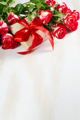 Red roses bouquet and present on wooden table.