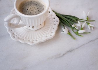 Simple spring background of beautiful white cup of coffee and snowdrops.