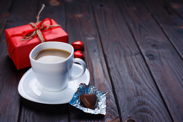 Valentine's Day concept. Cup of coffee with heart shaped chocolates and gift box on wooden table, copy space