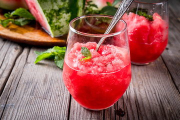 Summer fruit desserts, frozen cocktails. Ice cream granite from watermelon with mint, in portioned glasses, with slices of watermelon. On old rustic wooden table Copy space