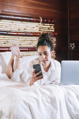 Pretty woman with phone and laptop in bed