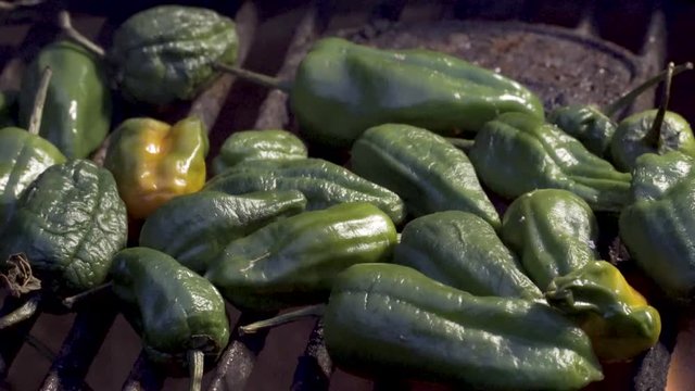 Flames licking padron peppers on the grill while the camera slides to the left.