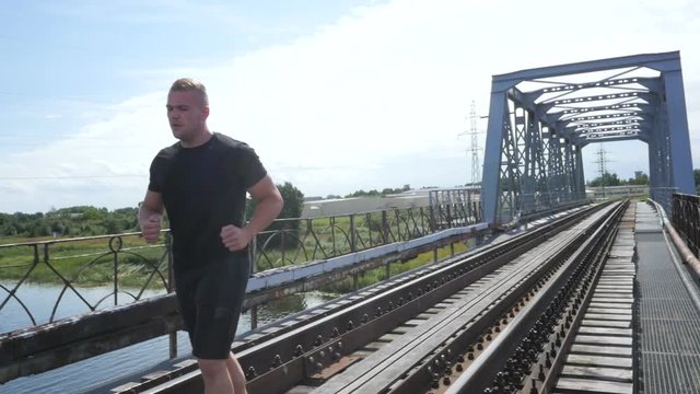 Athletic man running on the bridge, slow motion steadicam video