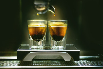 Professional coffee brewing. Coffee espresso. Close-up of espresso pouring from coffee machine to shotglasses.