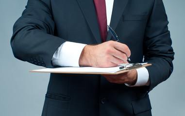 Businessman in suit is holding clipboard and pen