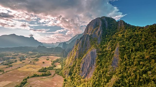 sun beam illuminates karst rocks at sunset time lapse aerial shot. rays of light over rice fields and limestone crags. Vang Vieng, Laos, view from the Pha Ngern View Point towards Tham Poukham Cave