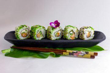 Green sushi rolls on a black rectangular elongated dish with chopsticks