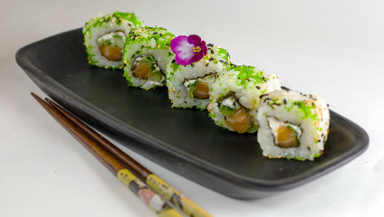 Green sushi rolls on a black rectangular elongated dish with chopsticks