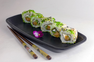 Green sushi rolls on a black rectangular elongated dish with chopsticks