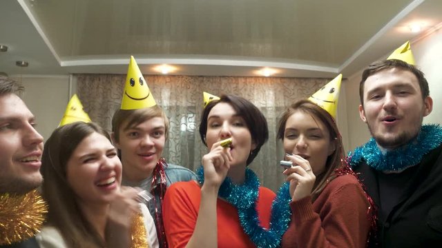 Friends with party hat blowing and having fun. Friends with party hats and festive noisemakers at party looking at camera and having fun. Young people having fun at birthday party