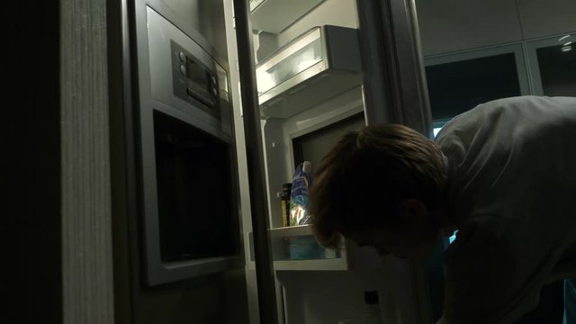 Portrait Of A Man Taking Food From Refrigerator. Portrait of a hungry man looking for food in refrigerator. Young happy man eating cake from the fridge