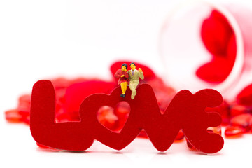 Miniature couple, sitting on LOVE text is wooden red color, using as Love of two people, valentine concept