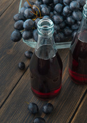 Glass bottles of fresh young red wine with a bunch of black grapes