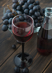 A wineglass of fresh young red wine with glass bottles and a bunch of black grapes