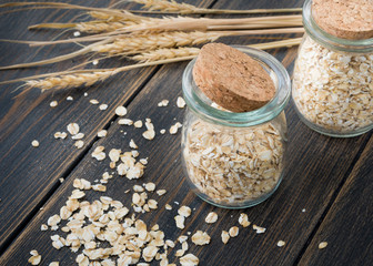 Raw oat flakes or oat ears cereals in craft glass jars with oat spikes or spikelets
