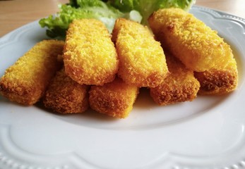 Close up of crisp fish fingers on a white plate; red and green oak vegetables on background; copyspace on bottom; perspective view