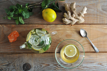 Glass teapot and glass mug of tea with ginger and lemon and mint on rustic wooden background