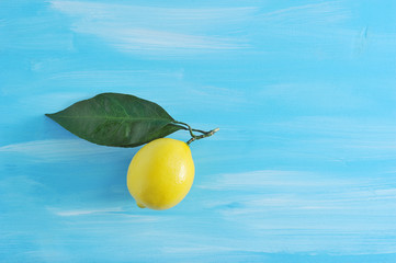 single fresh yellow lemon with leaves on blue wooden background