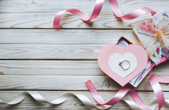 Marriage proposal concept. A wedding ring on a gift box on a wooden background. Valentine's Day. Copy space. Top view.