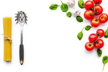 Cooking italian pasta. Spaghetti, tomatoes, garlic, basil and cookware on white background top view copyspace