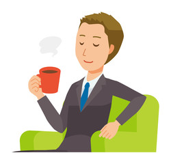 A young businessman is sitting on the sofa and drinking coffee