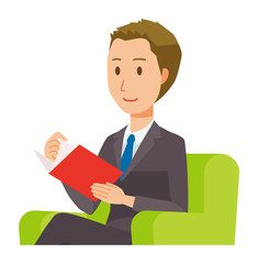 A young businessman is sitting on a sofa and reading books