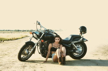Fototapeta na wymiar young woman in denim overalls , sitting on the ground near a motorcycle
