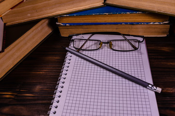 Notepad, eyeglasses and pencil in front of books