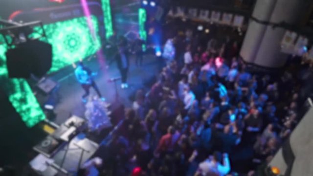 Concert in nightclub, blurred view of the crowd of dancing people, multicolored light.

