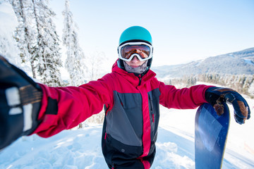 Fototapeta na wymiar Shot of a man snowboarder taking a selfie, wearing helmet, skiing mask and colorful winter snowboard clothing, standing on top of the mountain at the ski resort